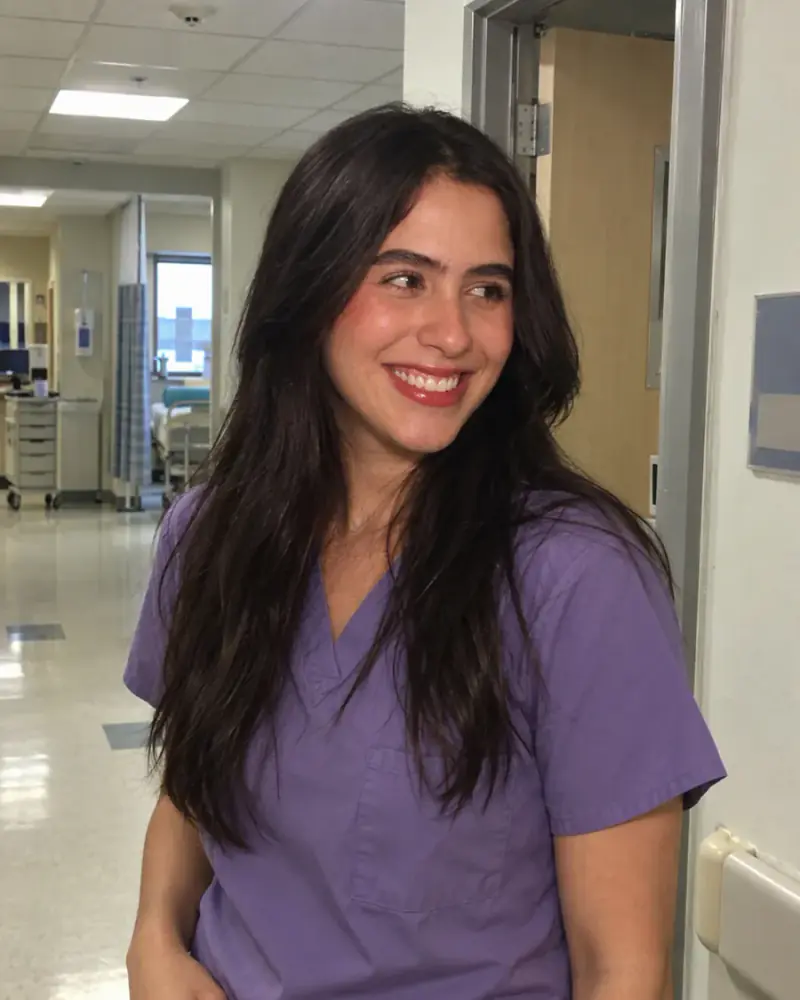 Clinician in purple scrubs smiling in a hospital corridor
